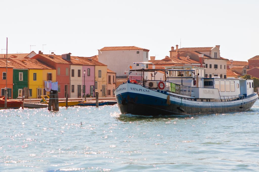 Barca "Vita Pugna" che naviga tra le colorate case storiche di Burano, Venezia, Italia.