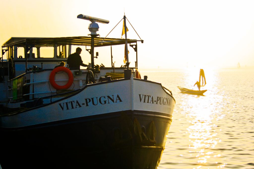 Barca "Vita Pugna" al tramonto mentre naviga nella laguna di Venezia, Italia.
