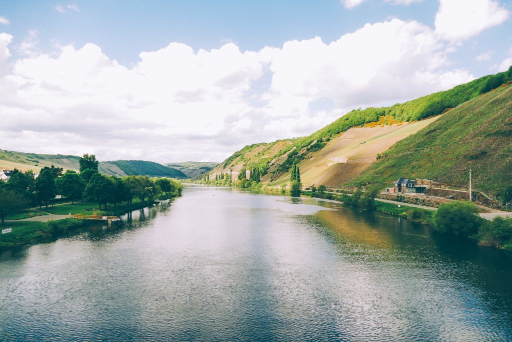 Mosel zwischen Weinbergen und Hügeln, mit blauem Himmel und Wolken, Deutschland.