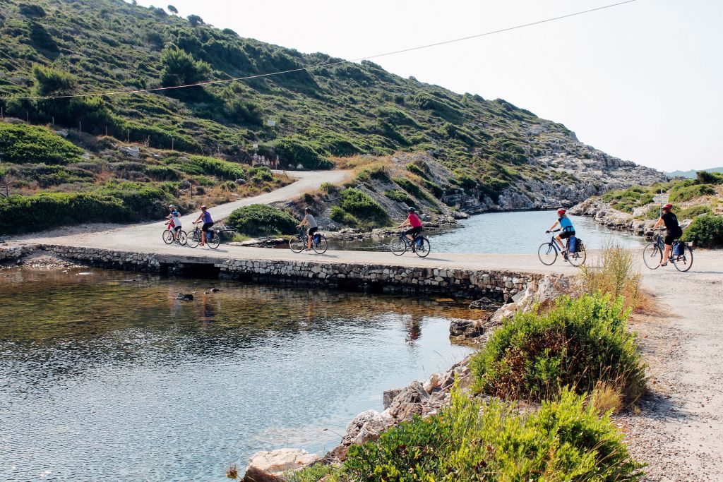 Hikers cross a path among Mediterranean vegetation, trekking in a group in Greece