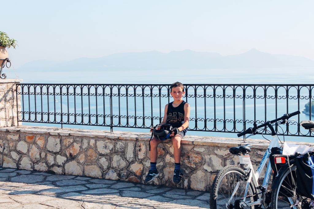 Ciclista in pausa su una terrazza con vista panoramica, belvedere con mare e monti, isole ioniche, Grecia