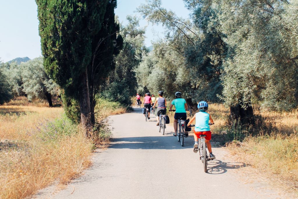Group on bike with "Girolibero" along a path among olive trees and Mediterranean vegetation, blue sky.
