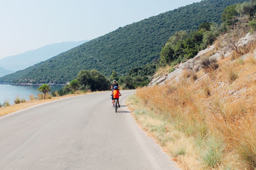 Cyclist traveling with "Girolibero" travels along a road along the coast with vegetation and hills.