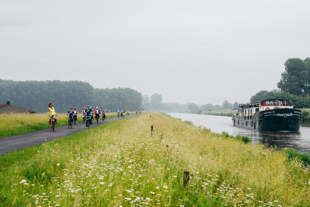 Barca "Magnifique III" che naviga sul fiume nei Paesi Bassi con ciclisti sulla pista ciclabile accanto