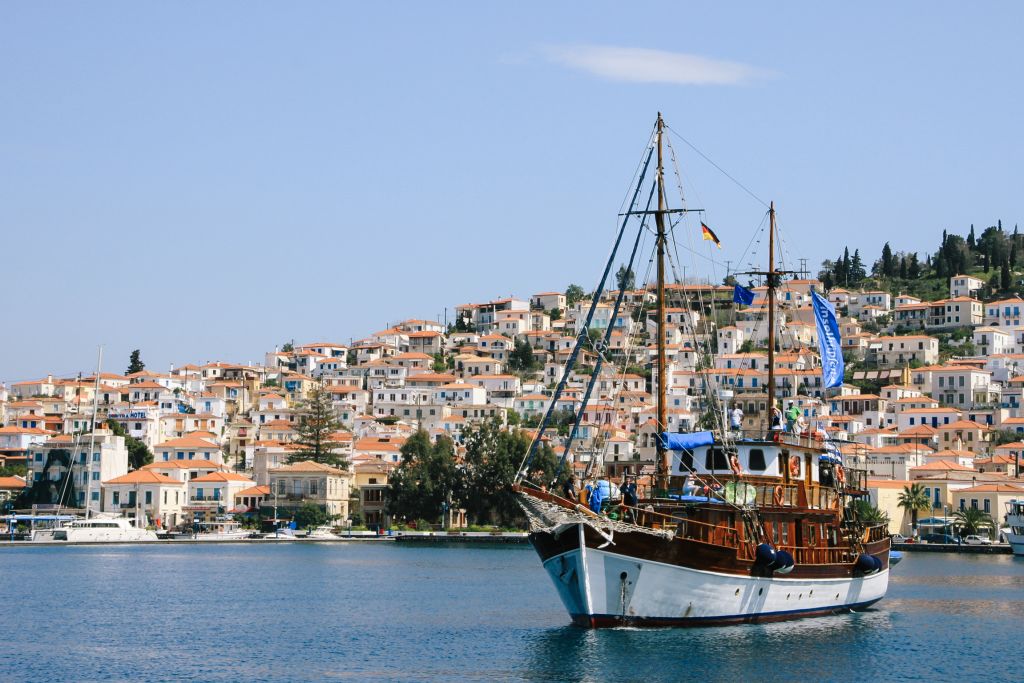 Wooden sailing boat anchored near a coastal town with traditional houses, Greece