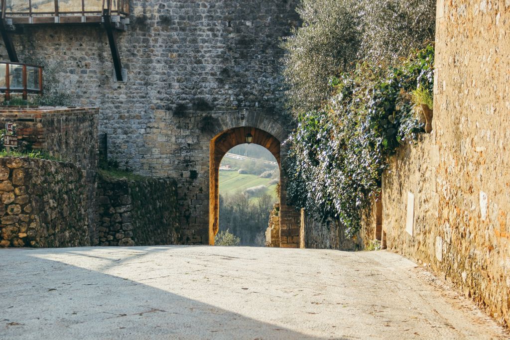 Antica porta in pietra di accesso alla città di Monteriggioni, lungo la Via Francigena in Toscana, con vegetazione sulle mura.
