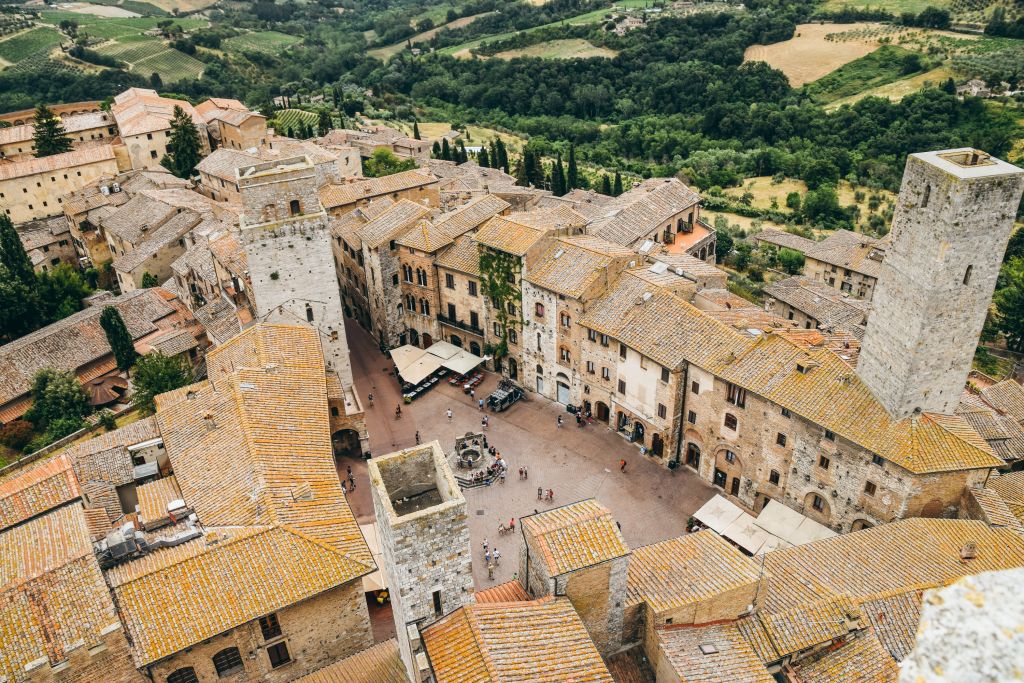 Vista dall’alto del borgo medievale di San Gimignano con tetti in terracotta e colline.