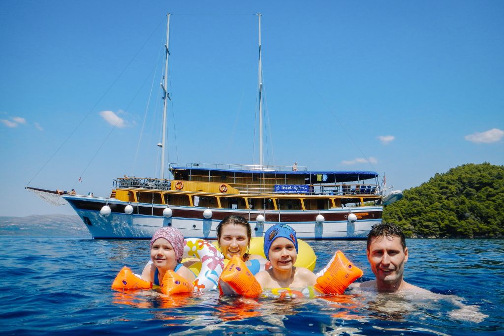 Famiglia con bambini che nuota nelle acque tranquille di una baia in Croazia, con dietro la barca "San Snova"