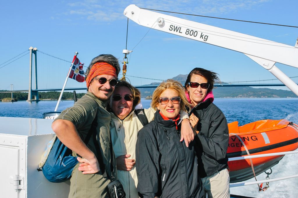 Gruppo di amici sorridenti in un porto turistico con barche sullo sfondo, Norvegia.