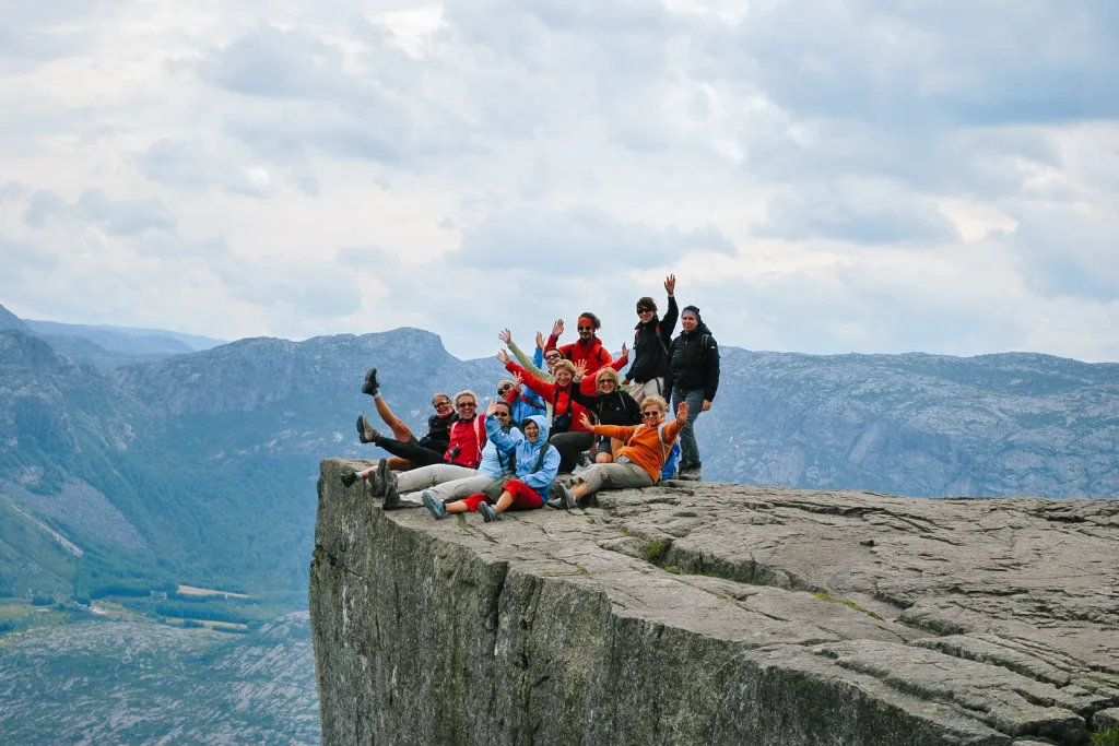 Gruppo di escursionisti seduti sulla cima di Preikestolen con vista sul fiordo, Norvegia, tour dei fiordi norvegesi