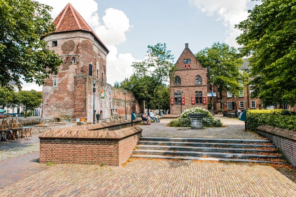 Piazzetta caratteristica con antica torre in un villaggio olandese, circondata da alberi