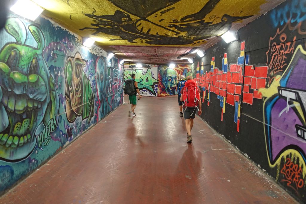 Escursionisti percorrono un sottopassaggio pedonale con graffiti colorati