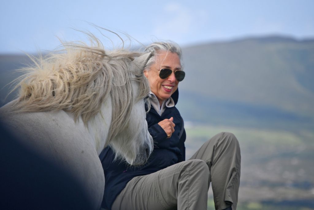 Donna accarezza un cavallo in un paesaggio rurale irlandese.