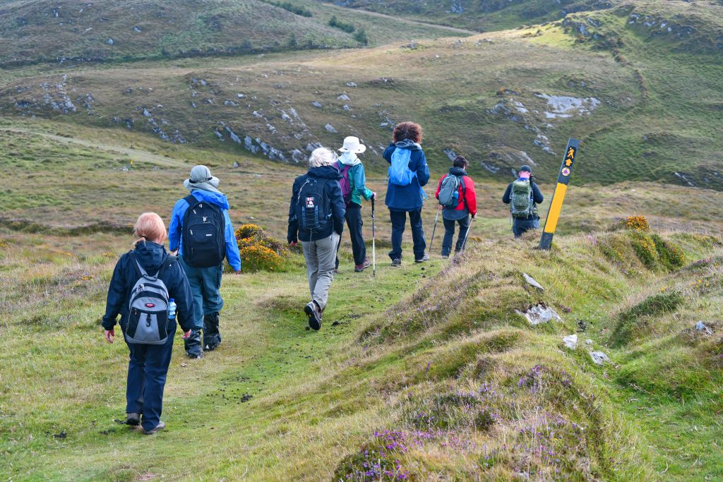 Gruppo di escursionisti che attraversa una valle erbosa, vacanze trekking "Girolibero"
