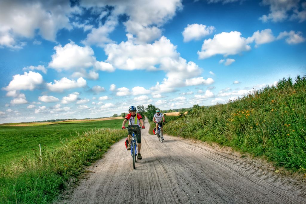 Ciclisti su una strada tra campi verdi e colline, paesaggio tipico dei Laghi Masuri, Polonia.