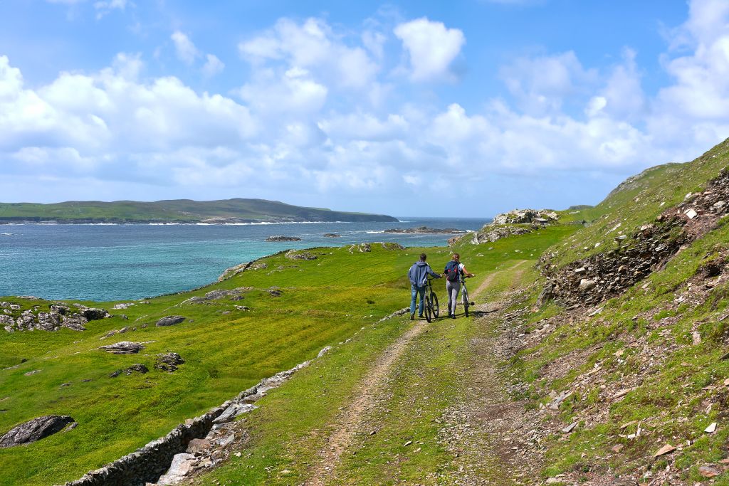 Sentiero escursionistico verde e collinare sull'isola di Inishbofin, Irlanda, con il mare in lontananza.