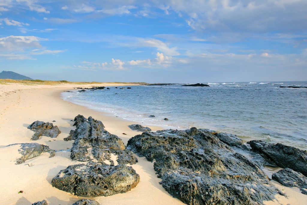 Scogliere rocciose e sabbia dorata lungo la costa atlantica nel nord del Portogallo, con mare calmo.