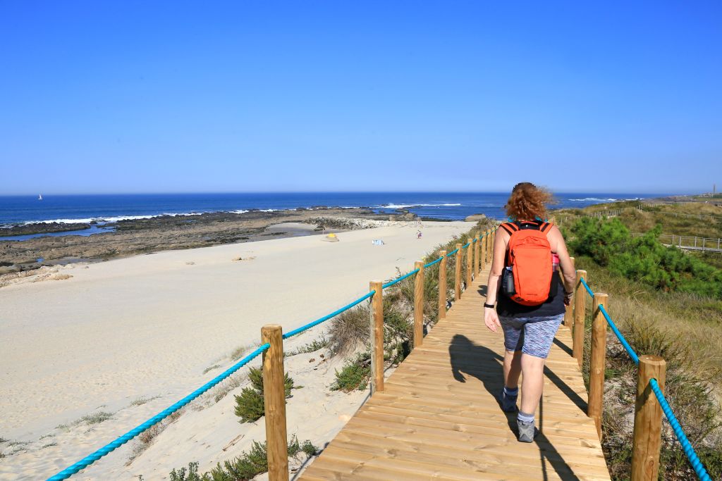 Escursionista con zaino che percorre una passerella lungo la spiaggia, ammirando l'oceano nel nord del Portogallo.