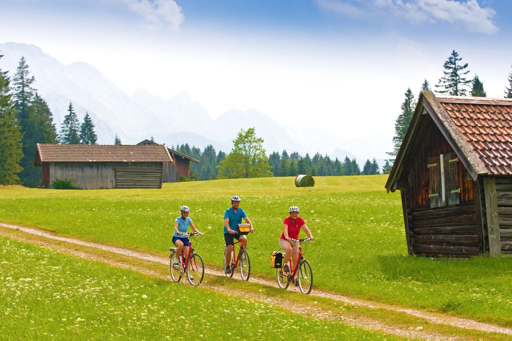 Gruppo di ciclisti su un sentiero rurale tra prati e baite alpine in Baviera, viaggi in bici "Girolibero"