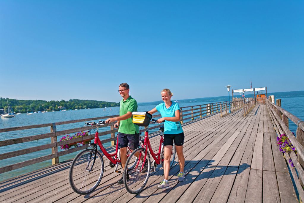 Ciclisti su un pontile di legno che si affaccia su un lago alpino in Baviera, Germania.