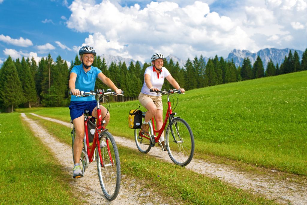 Coppia in bicicletta su un sentiero verde tra prati e colline bavaresi, Germania, in una giornata soleggiata.