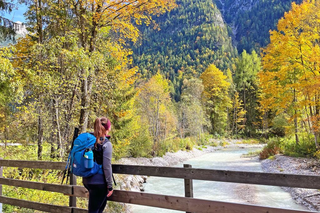 Escursionista lungo un fiume circondato da alberi dai colori autunnali, natura incontaminata, vacanze in montagna, Baviera.