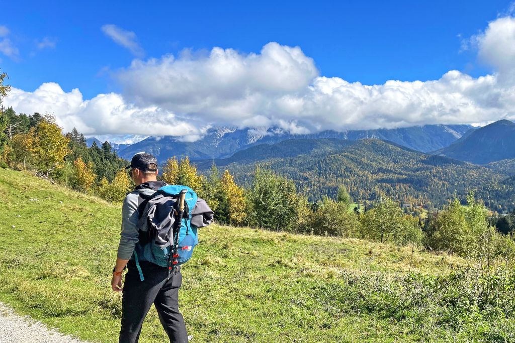 Escursionista che cammina in un campo aperto con lo Zugspitze sullo sfondo.