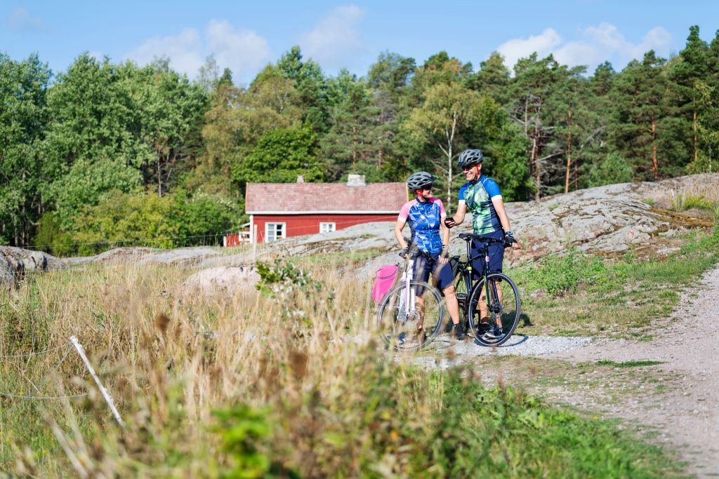 Coppia in bicicletta su una strada sterrata vicino a una casa rossa tradizionale finlandese tra i boschi