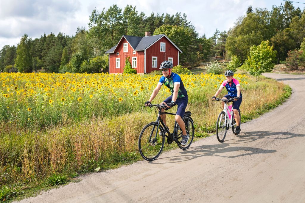 Coppia in bicicletta lungo un sentiero circondato da prati e boschi, nell'arcipelago di Turku.