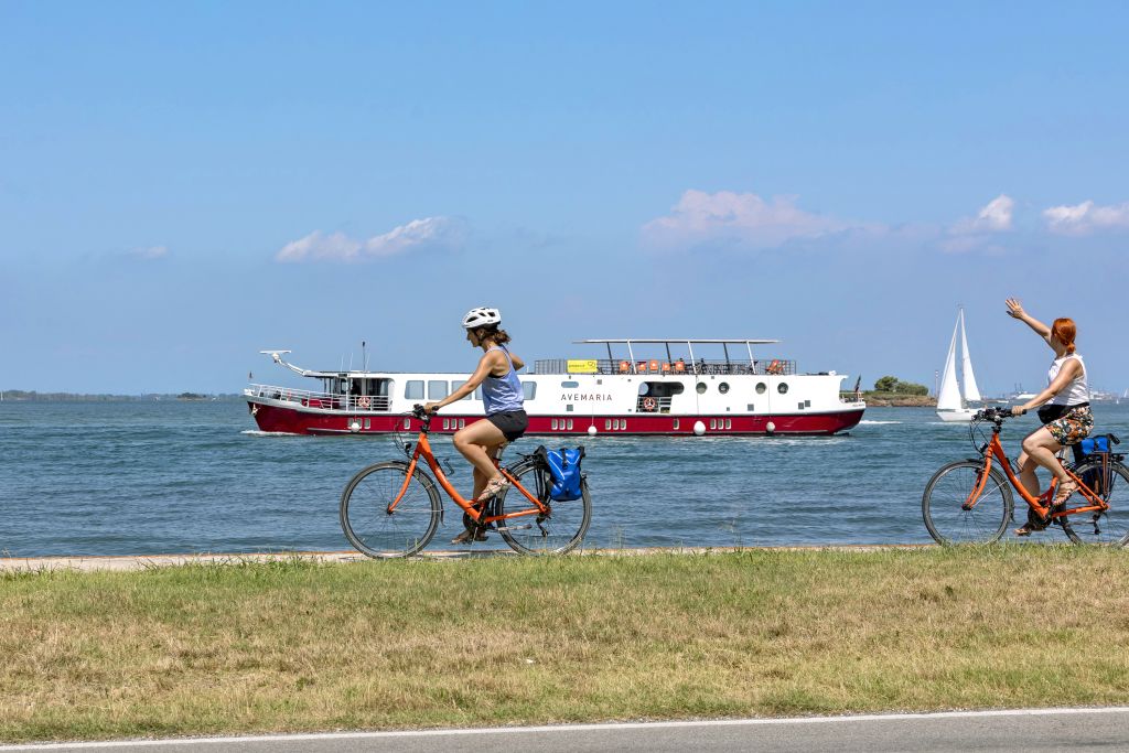 ciclisti sulla ciclabile nella laguna veneta con barca Ave Maria in navigazione sullo sfondo