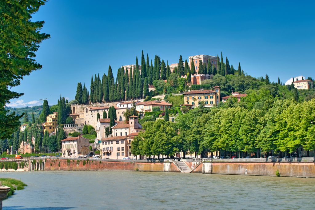 Ciclabile con vista sul fiume Adige e sull'altra sponda un bel paesaggio con cittadina medioevale sul colle con cipressi, viaggiare in bicicletta, paesaggi del Veneto