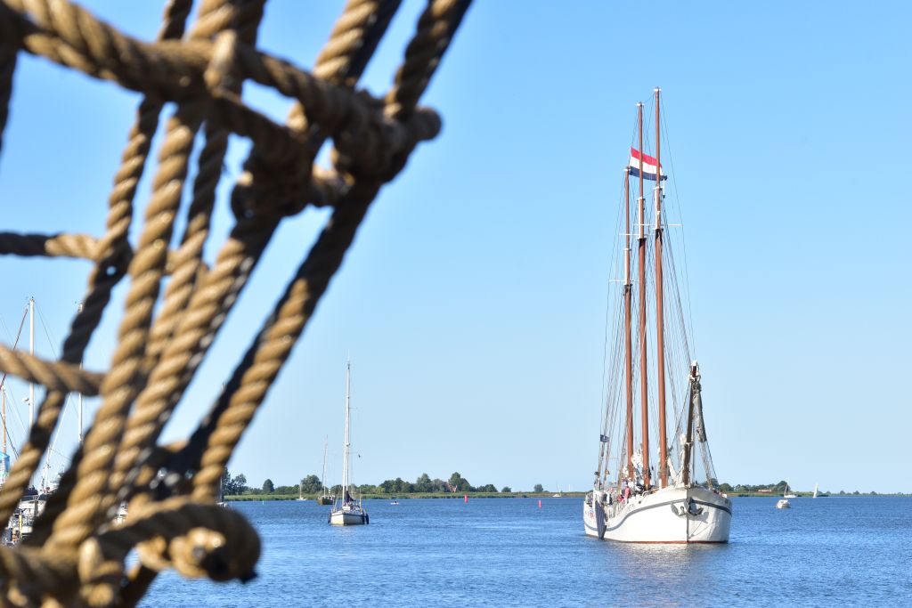Barca a vela bianca naviga nei canali olandesi, vista parziale con corde in primo piano.
