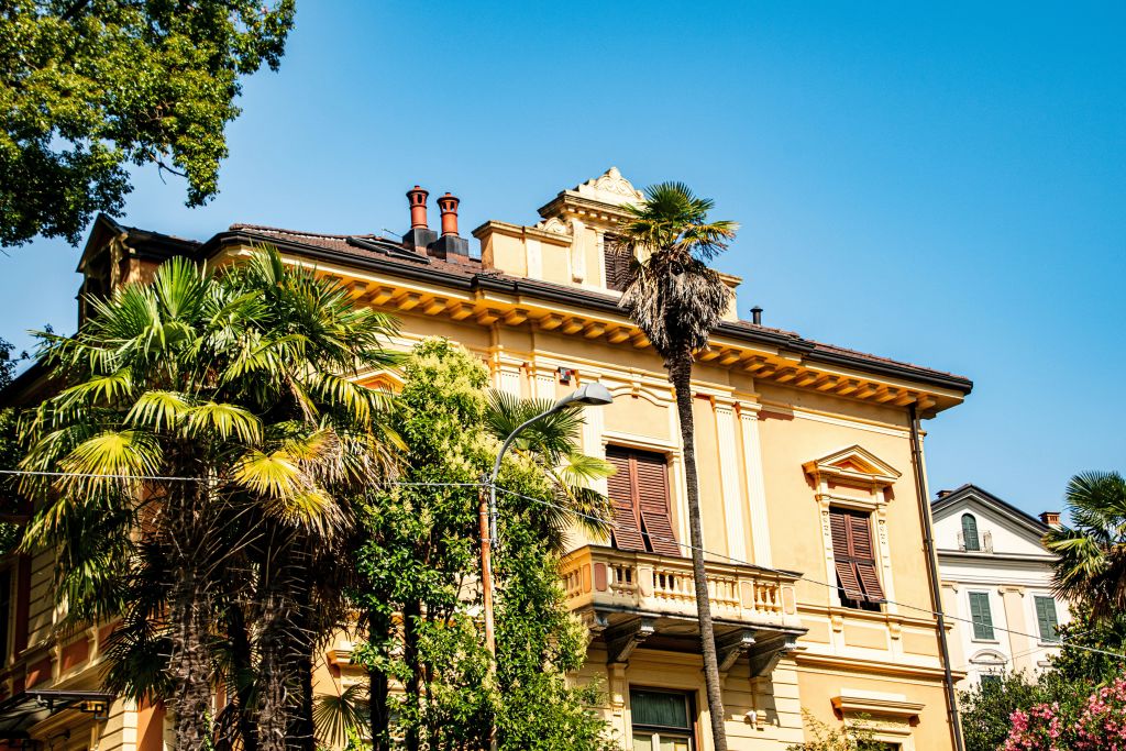 Villa storica a Verbania sul Lago Maggiore, circondata da palme e vegetazione lussureggiante, sotto un cielo azzurro.