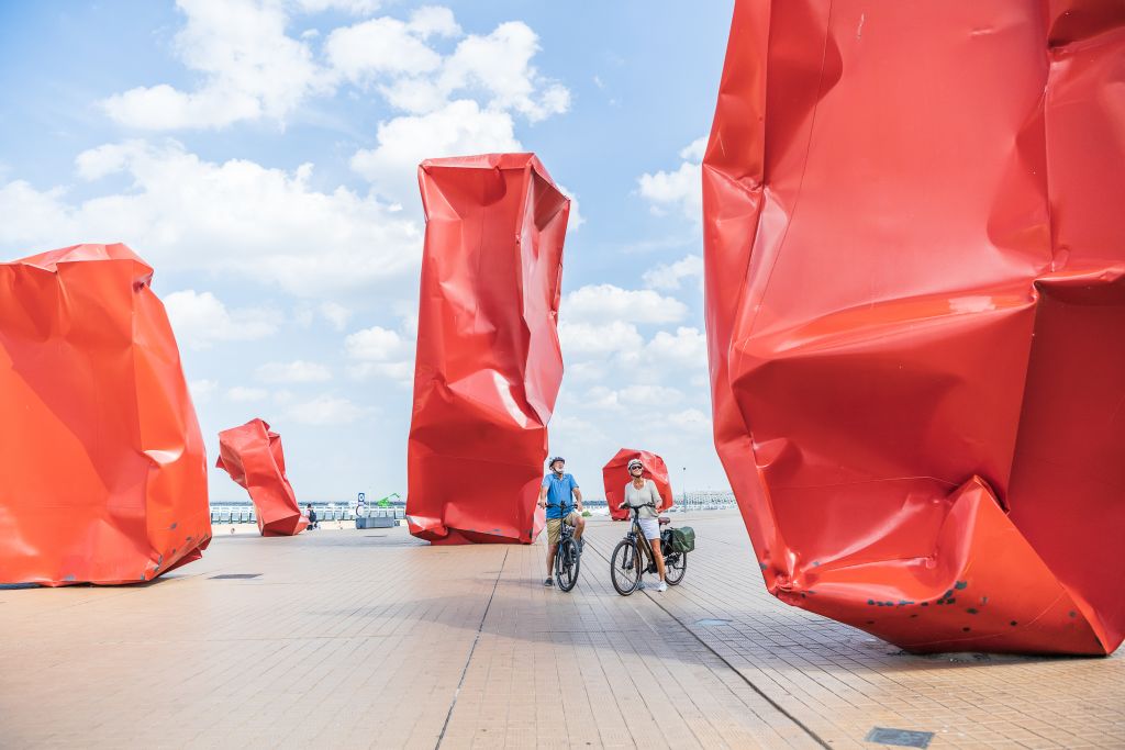 Sculture rosse moderne a Oostende, Belgio, con famiglie in bicicletta in viaggio con Girolibero lungo il mare.