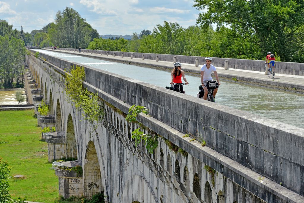 Ciclisti in viaggio con Girolibero sul ponte-acquedotto di Agen, Garonna, Francia, immersi nel paesaggio verde circostante.