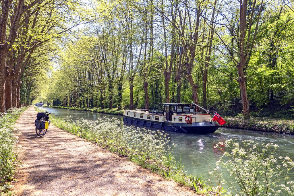Bici parcheggiata su una ciclabile accanto a un canale alberato lungo il canale della Garonna, Francia.
