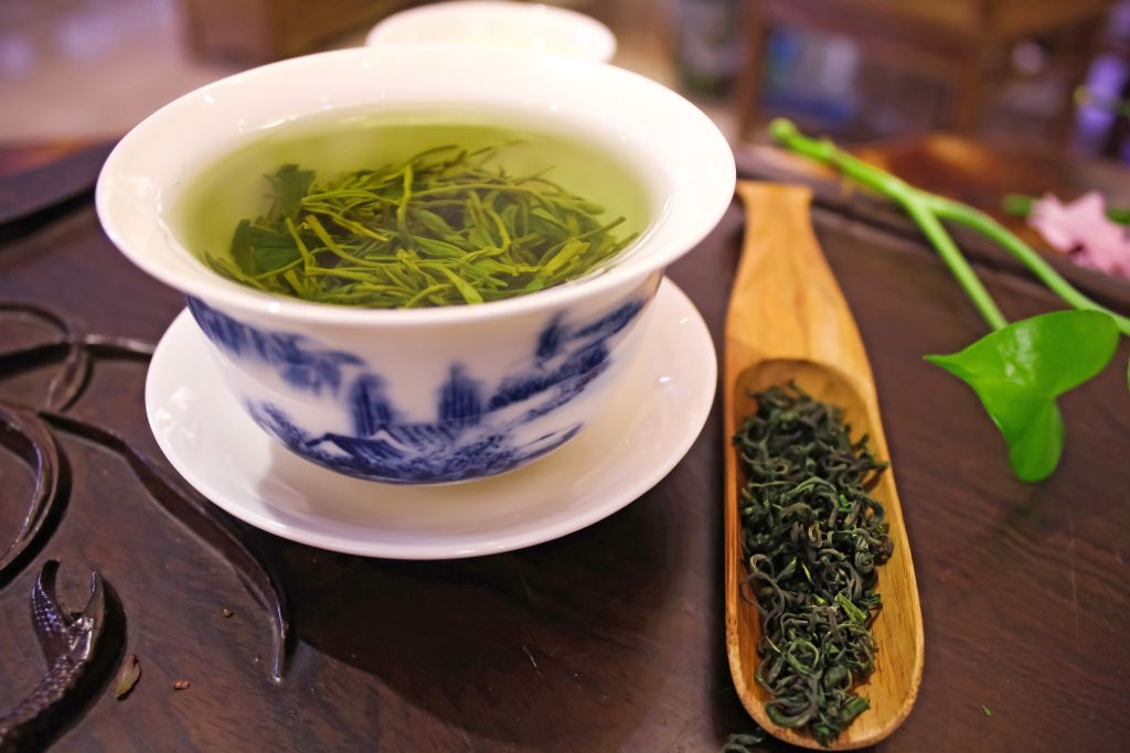 Tazza di tè verde Longjing su tavolo in legno con foglie fresche, Cina.