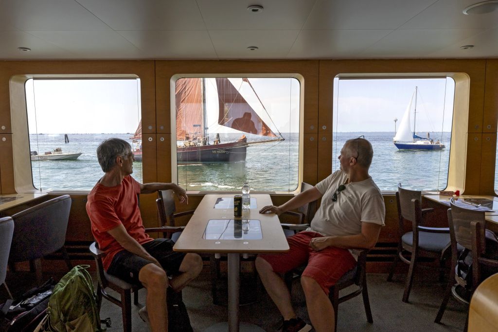Coppia seduta al tavolo interno della barca con finestre con vista sul mare