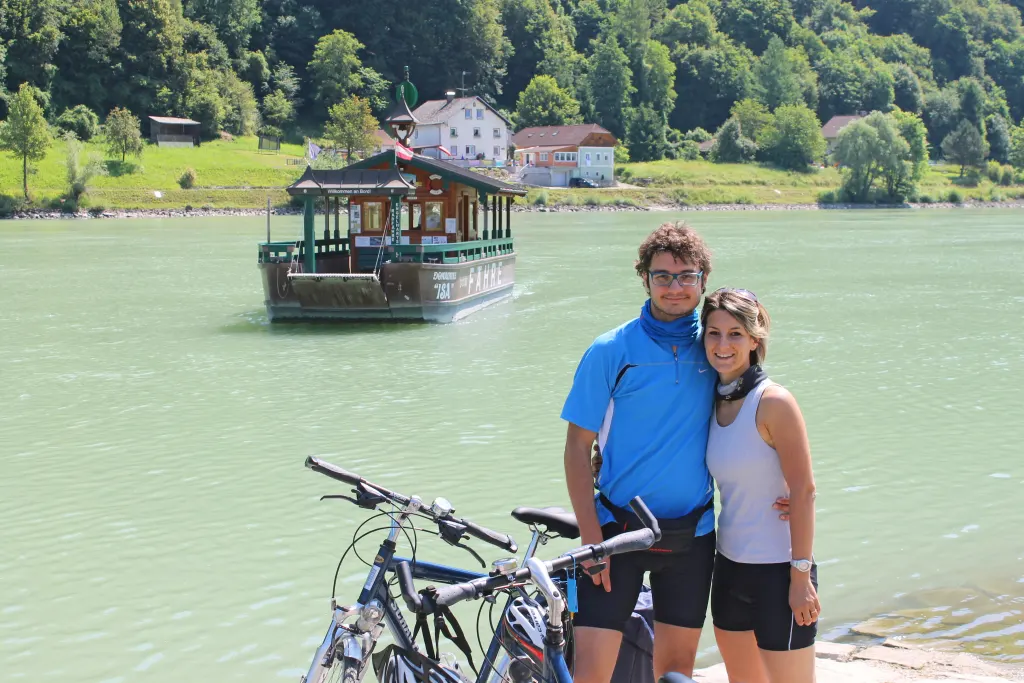 Coppia con biciclette sulla riva del fiume Inn a Passau, davanti alla famosa locanda sull’acqua.