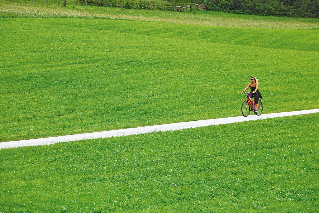 Ciclista che pedala su un sentiero ciclabile tra i prati verdi nella regione di Salisburgo.