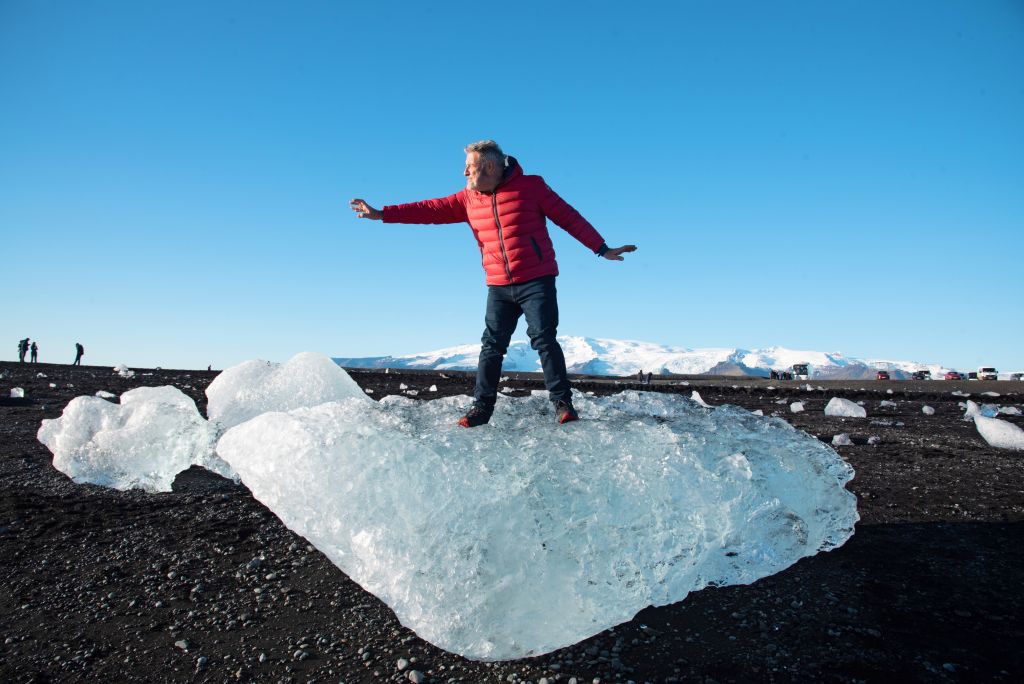 Persona in piedi su un blocco di ghiaccio nella laguna glaciale di Jökulsárlón, con un cielo limpido, Islanda.