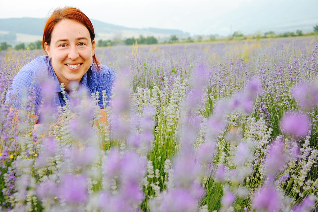 Donna sorridente in un campo di lavanda in fiore, circondata da profumi e colori estivi.