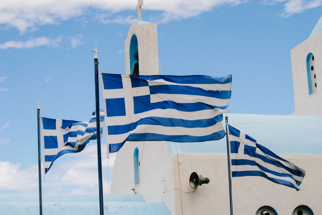 Greek flags waving above a white church in the Cyclades, Greece.