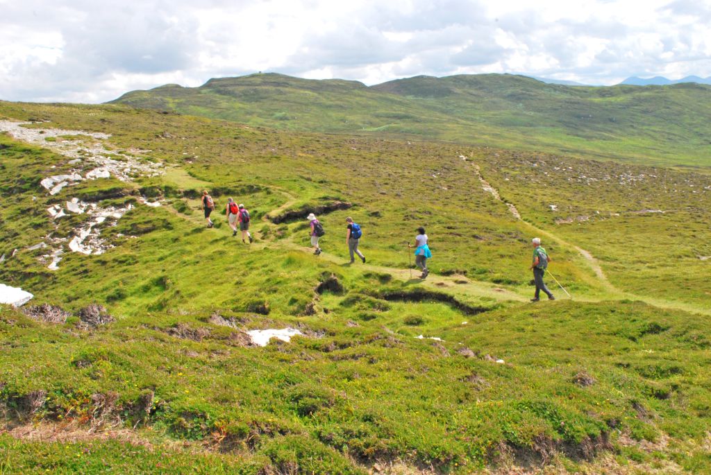 Escursionisti lungo un sentiero che attraversa un vasto paesaggio collinare verde in Irlanda, viaggi trekking