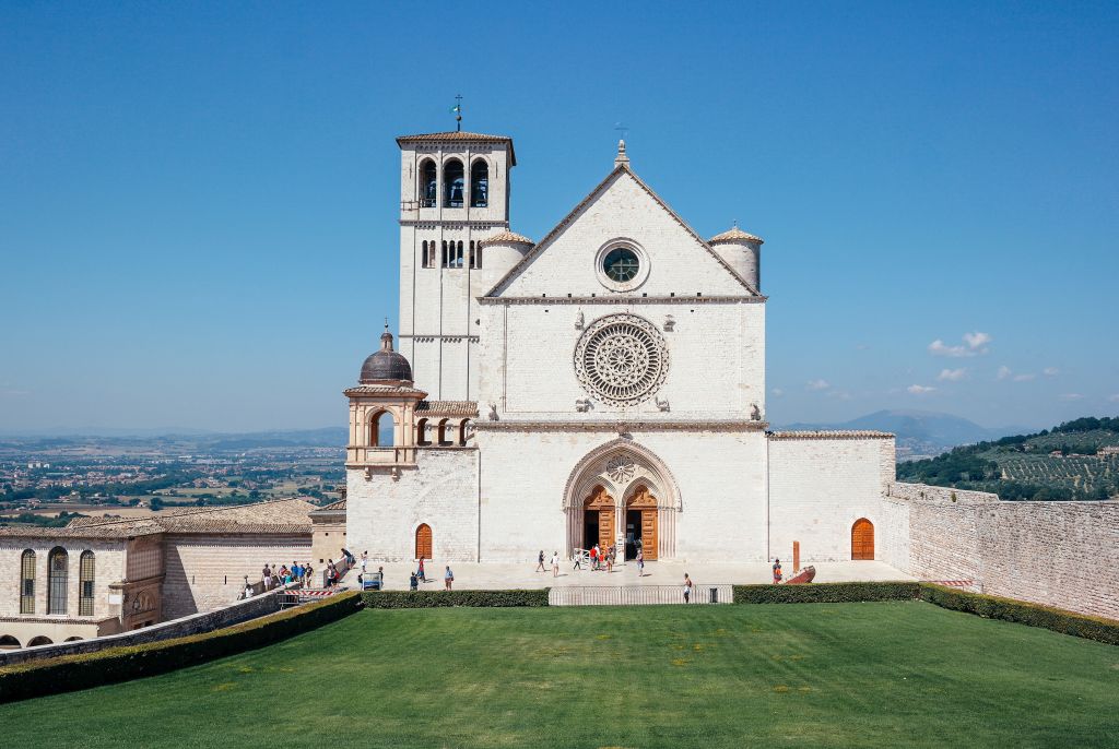 Vista sulla facciata della Basilica di San Francesco ad Assisi con prato verde e cielo sereno