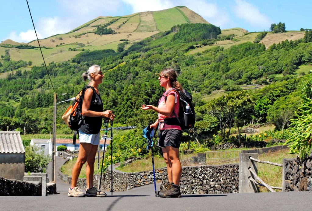 Due escursionisti con zaini camminano lungo una strada panoramica circondata dal verde nelle Azzorre.