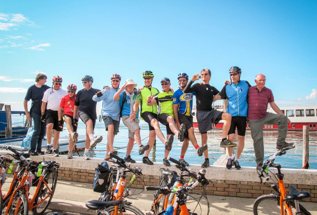 Organised group trips Girolibero, group of smiling cyclists with their bikes on a sunny terrace
