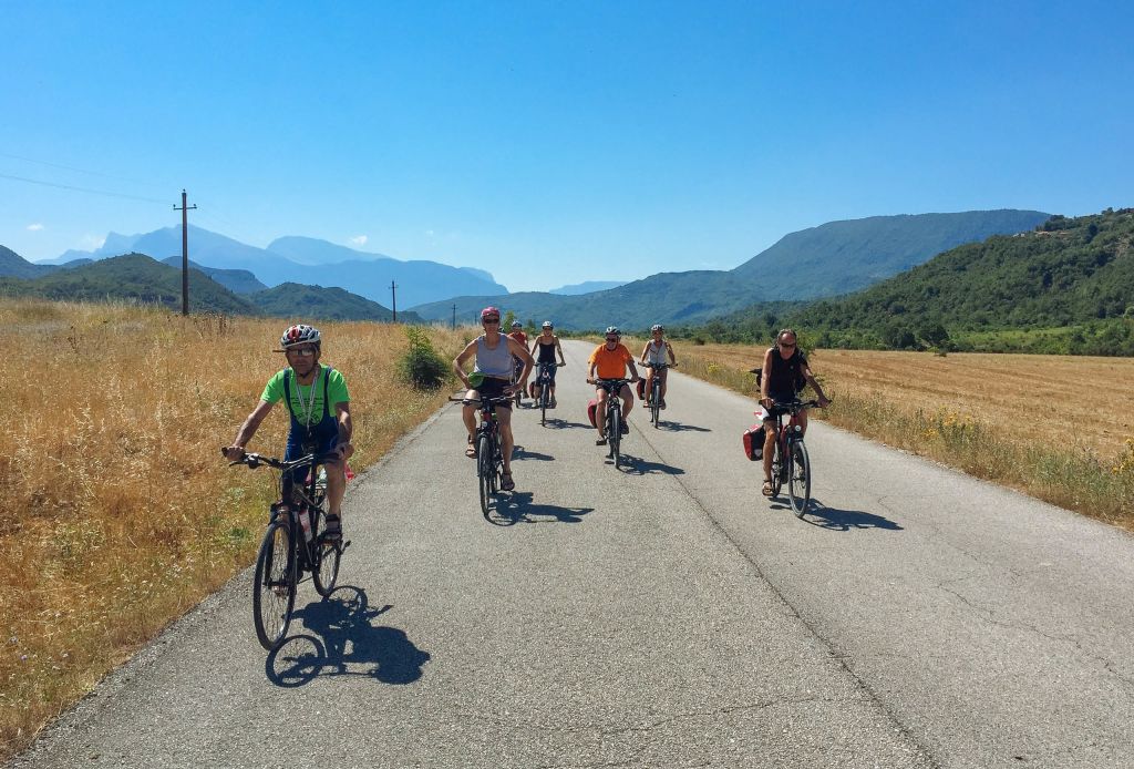 Gruppo di ciclisti che percorre una strada panoramica tra colline in Albania.