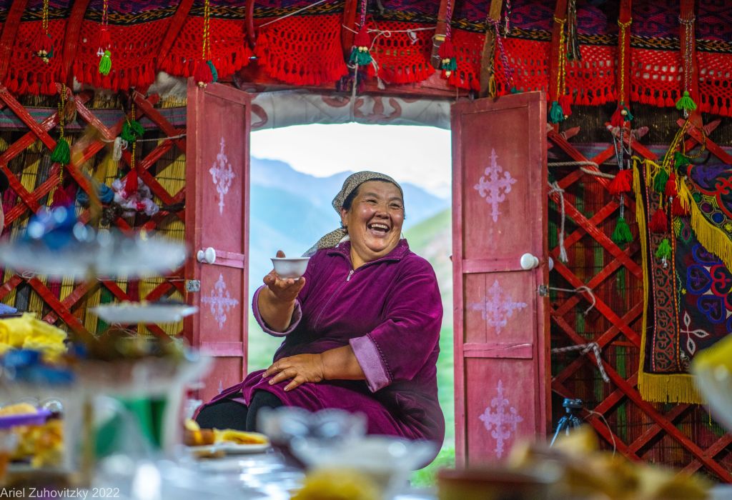 Donna locale in abito tradizionale kirghiso sorride seduta in una yurta decorata con tessuti variopinti, Kirghizistan