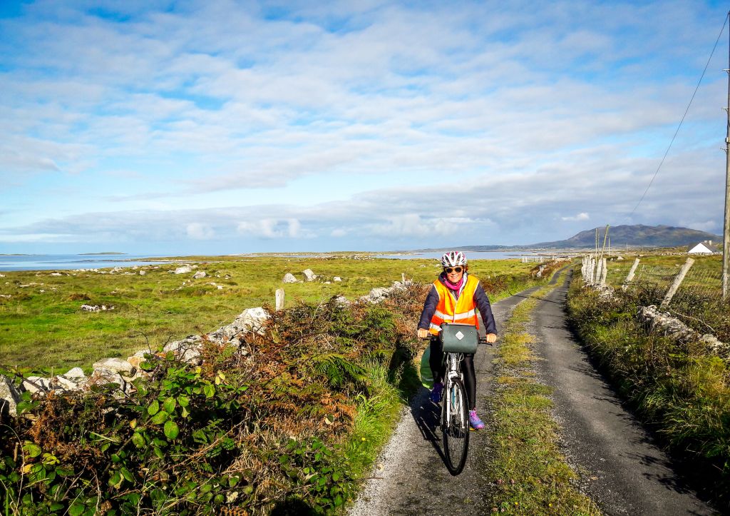 Ciclista su un sentiero costiero nel Connemara, Irlanda, con paesaggio di prati e colline.